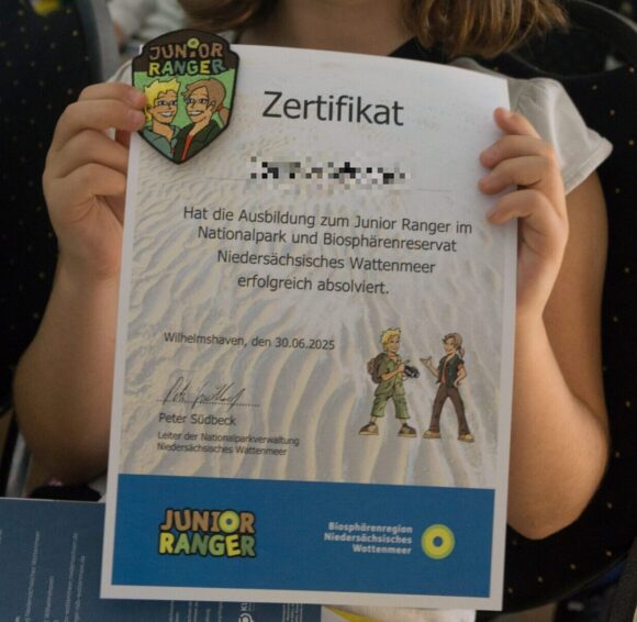 Eine Schülerin zeigt ihr Zertifikat und das Junior-Ranger-Abzeichen.